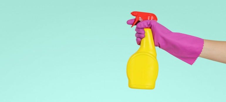 A hand with pink rubber glove holding a yellow spray bottle